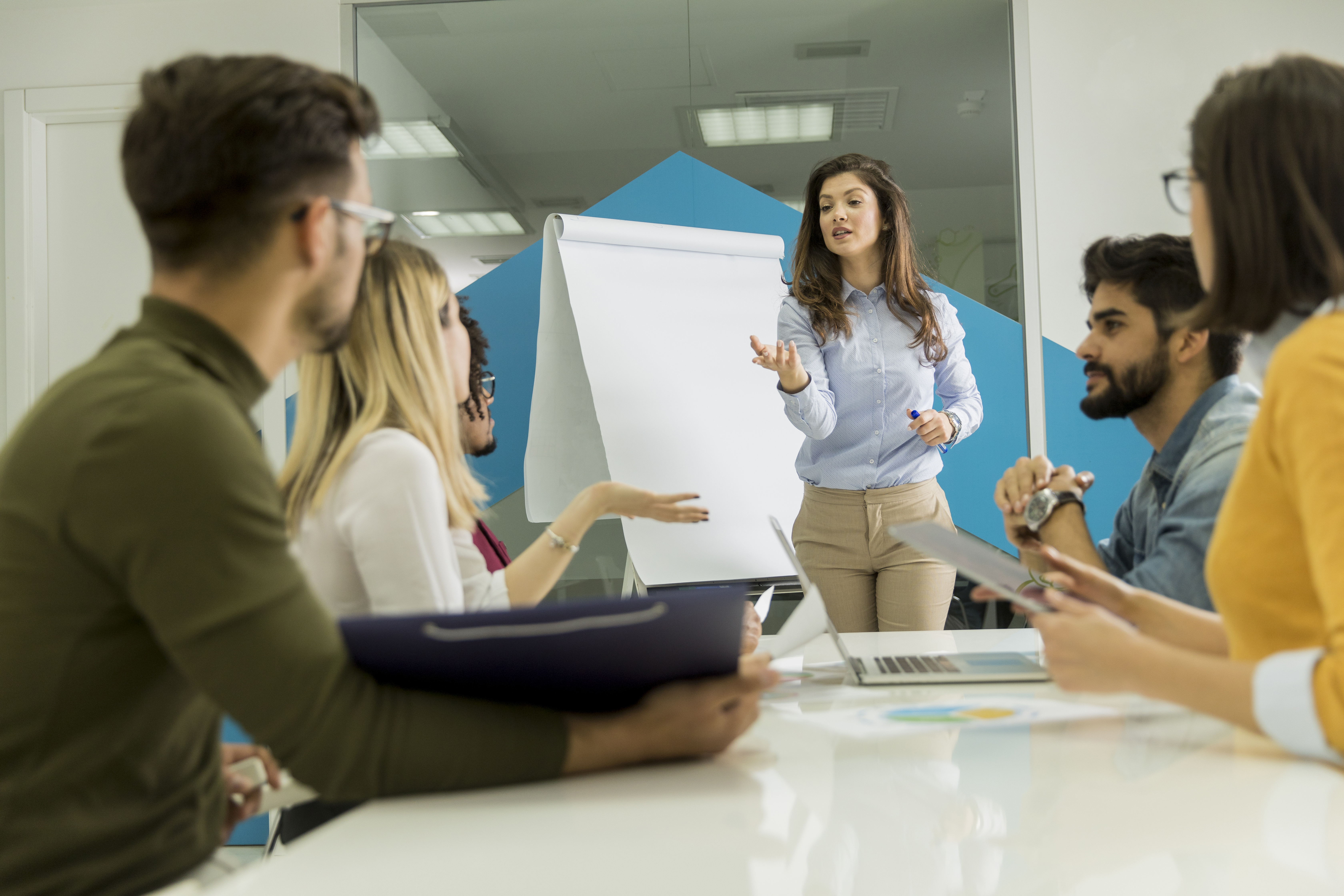 A group of students sitting around a table with a woman standing up giving instruction