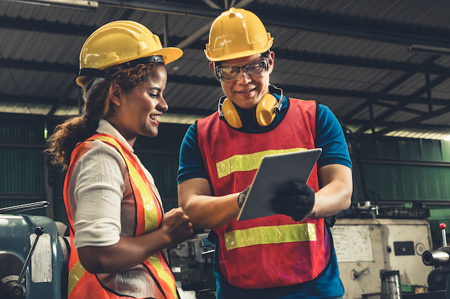 An instructor in safety gear is showing a student, also in safety gear, information on a clipboard