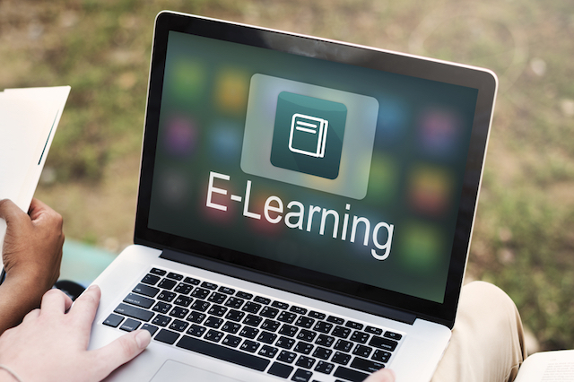 Close up of a person’s hands holding a laptop. The laptop’s screen features an icon of a book with the word “e-learning” written below. 