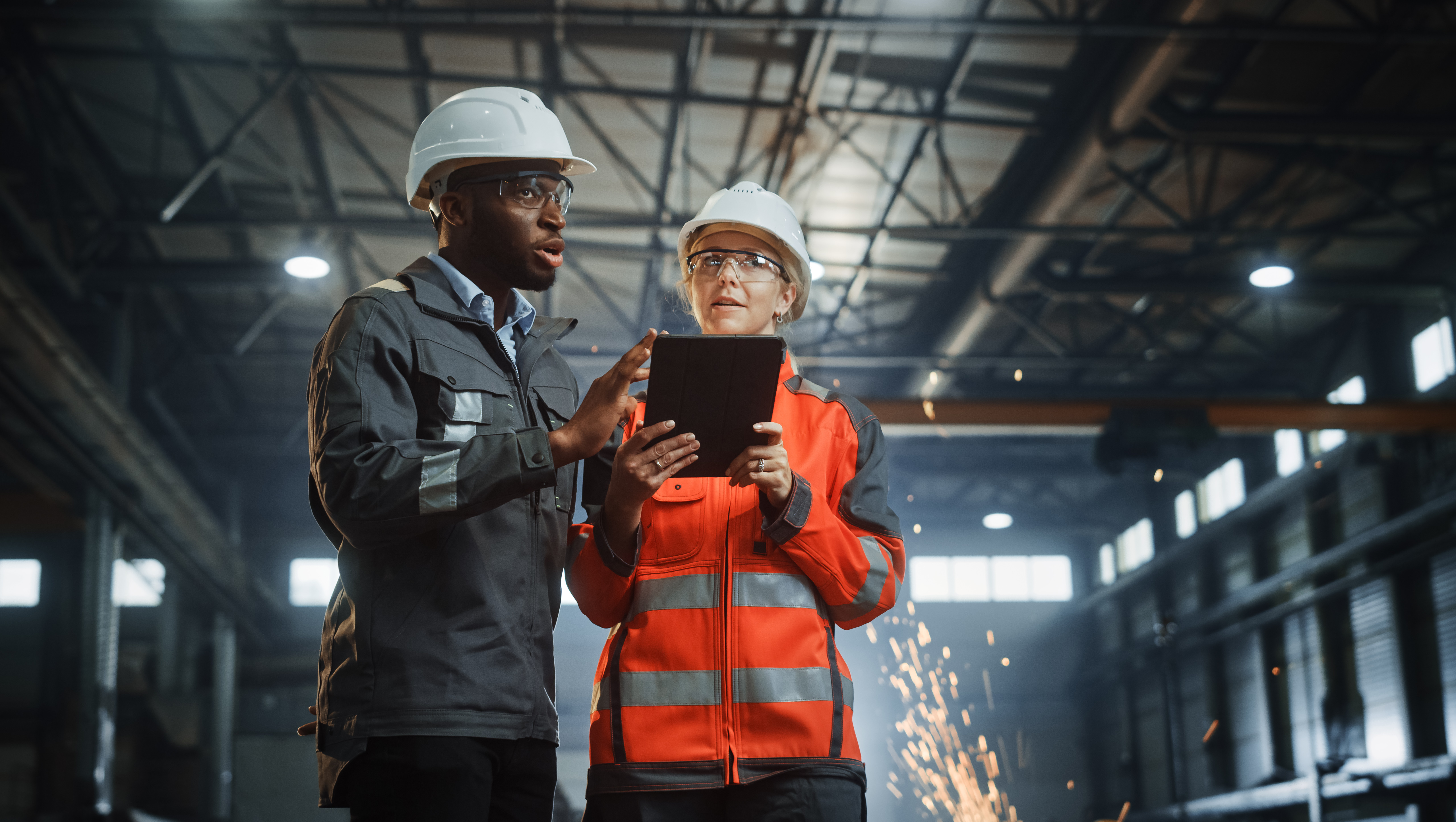Two people wearing safety gear discussing something on an ipad.