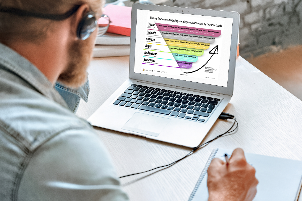 A man sitting in front of a laptop with a graphic explaining what Bloom’s Taxonomy is on the screen.